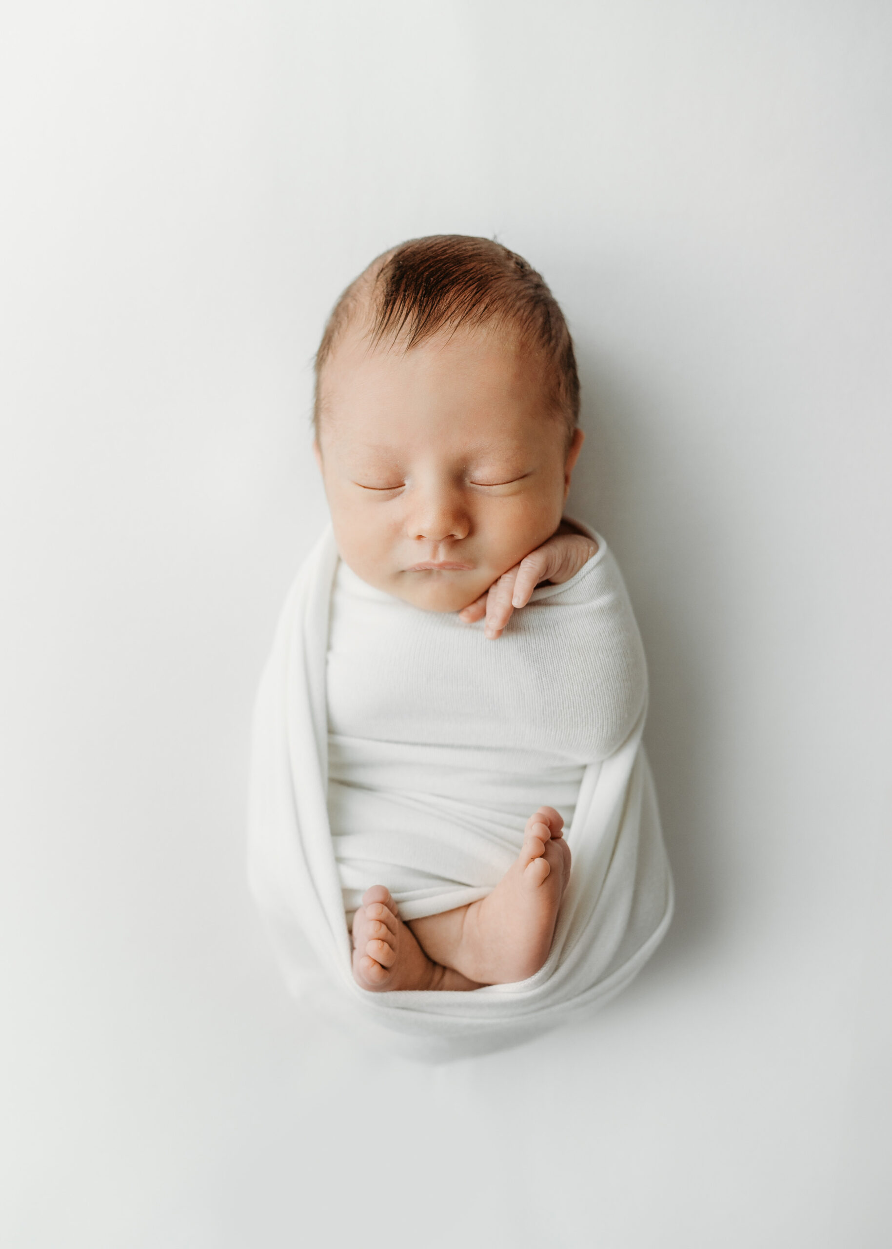 A baby boy is swaddled in a white blanket and asleep during his newborn session in Atlanta.