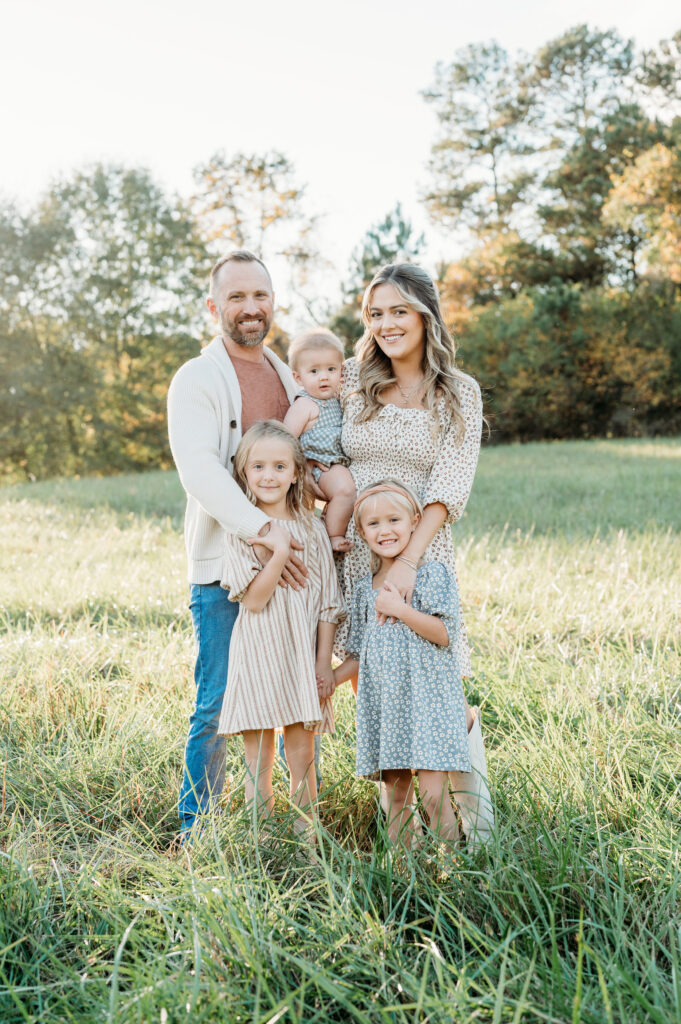 Family Session at Birmingham Park in Milton, GA in the sunset and all family members are looking into the camera smiling.