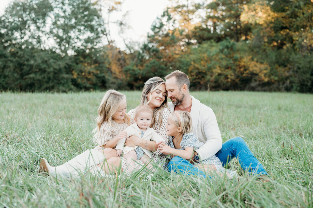 The family is sitting on a blanket in the grass and smiling during a family session in Birmingham Park, Atlanta