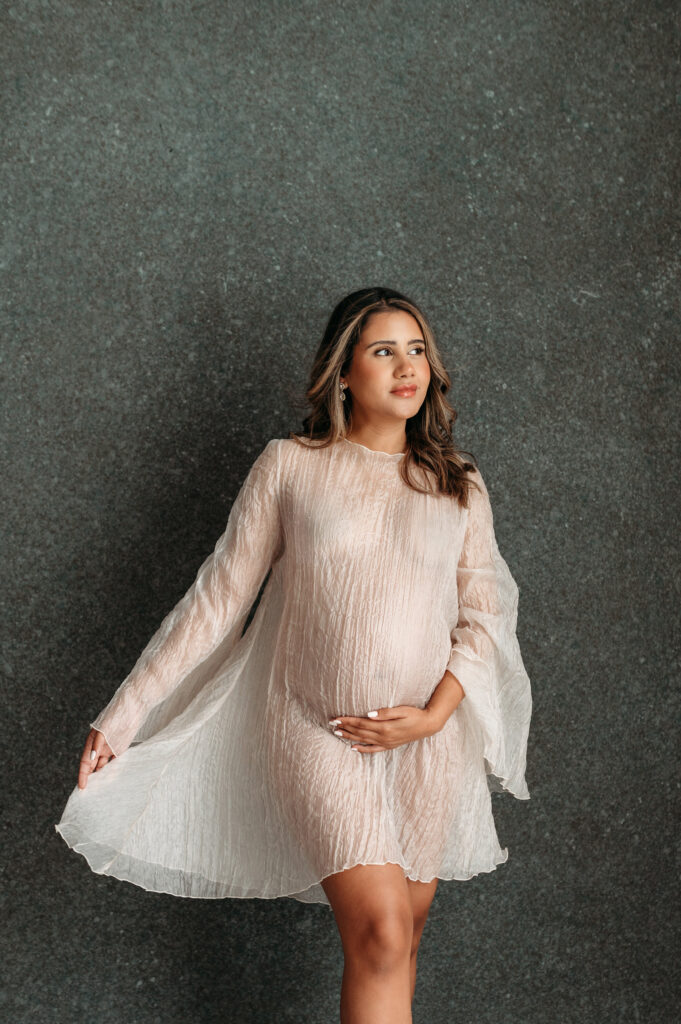 Pregnant mama in light chiffon dress sstanding holding her hand under her belly in her studio maternity session in Atlanta