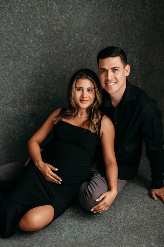 Pregnant mama in black dress sitting close to her husband in her studio maternity session in North Atlanta