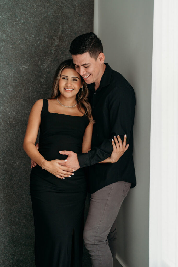 Pregnant mama in black dress standing close to her husband in her studio maternity session in Atlanta